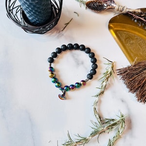 May include: A black lava rock bracelet with iridescent beads and a small charm in the shape of a witch's hat.