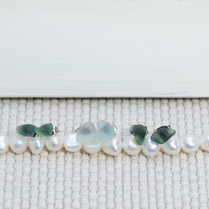 May include: Three pairs of earrings featuring sea glass and silver settings. The earrings are displayed on a white pearl necklace.