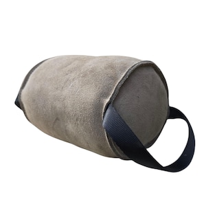 May include: A grey suede-like cylindrical object with a black handle. The object has a rounded shape and appears to be made of a soft material. The black handle is a loop attached to the side of the object.