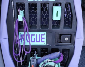 May include: A purple and black dog crate with a sign that says "Working Dog Stay Back". The crate has a blue and purple leash hanging from a hook, a blue and purple collar, a blue and purple rope, a blue and purple dog tag, a blue and purple dog treat dispenser, and a blue and purple dog waste bag dispenser. The crate also has a blue and purple nameplate that says "Rogue".