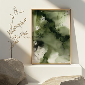 May include: Abstract green and black watercolor painting in a gold frame on a white shelf with two gray rocks.