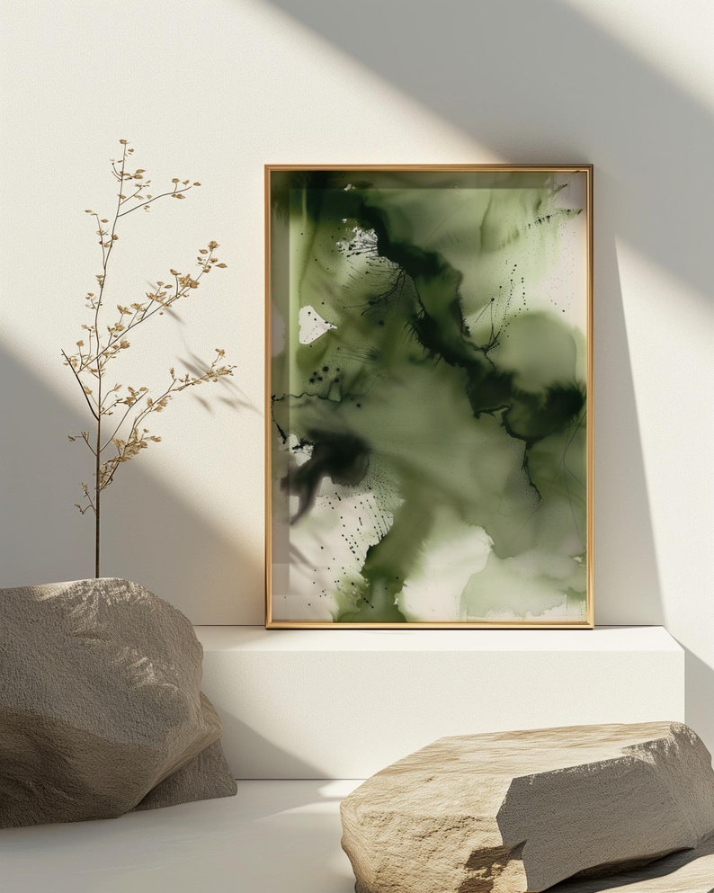 May include: Abstract green and black watercolor painting in a gold frame on a white shelf with two gray rocks.
