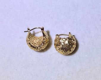 May include: A pair of gold hoop earrings featuring a textured, cross-hatched surface pattern. The earrings are small, semi-circular in shape, and include a hinged post mechanism for secure closure. The metal has a bright, reflective finish.