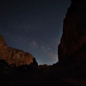 May include: A night landscape featuring a dark blue sky filled with numerous stars. Two large, dark rock formations frame the starry sky, creating a dramatic contrast. The scene evokes a sense of vastness and the beauty of the night.