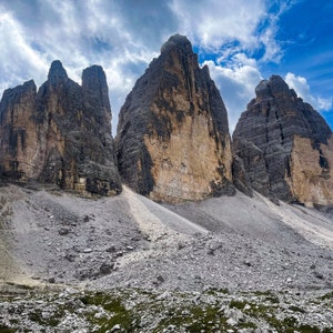 May include: Three towering rock formations rise against a cloudy sky. The rock faces are a mix of gray and brown, with a light dusting of snow on the ground.