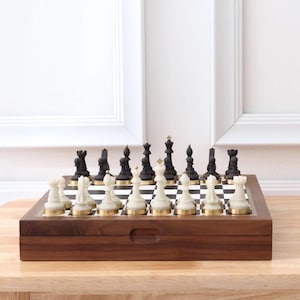May include: A complete chess set with black and white pieces on a checkered board. The chess pieces are set up on a wooden board with a dark brown finish. The chess pieces have gold accents.