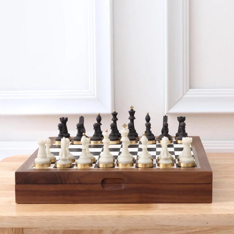 May include: A complete chess set with black and white pieces on a checkered board. The chess pieces are set up on a wooden board with a dark brown finish. The chess pieces have gold accents.
