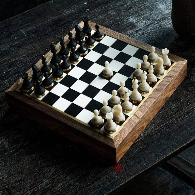 May include: A wooden chess set with black and white pieces arranged on a checkered board. The chess pieces are black and white with gold-colored accents. The board is set in a wooden frame.
