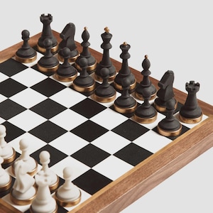 May include: A chess set with black and gold pieces on a black and white checkered board. The chess pieces are black with gold-colored bases. The board is set in a wooden frame.