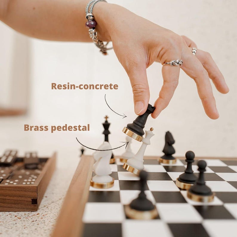 May include: A chess set with black and white resin-concrete pieces and brass pedestals. The board is black and white checkered. The text "Resin-concrete" and "Brass pedestal" are visible.