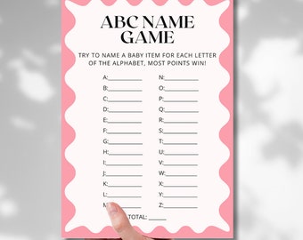 May include: A pink and white baby shower game card with the text "ABC NAME GAME". The card has a wavy pink border and prompts players to name baby items for each letter of the alphabet. The game is held by a hand.