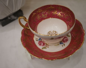 Pode incluir: Um conjunto de chávena e pires de chá rosa e dourado com desenhos florais. A chávena tem um interior branco e uma borda dourada. O pires tem uma borda ondulada.