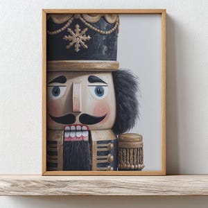 May include: A framed print of a wooden nutcracker soldier. The nutcracker has a black hat with gold accents and a snowflake design. It has a light-colored face, blue eyes, a black mustache, and a red mouth. The frame is a light brown color.