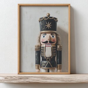 May include: Framed print of a wooden nutcracker soldier. The nutcracker is dressed in a black uniform with gold accents, a black hat with a gold star, and a large mustache. The print is in a wooden frame and sits on a wooden shelf.