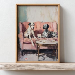 Puede incluir: Una impresión enmarcada con dos perros dálmatas en un sofá rosa, jugando a las cartas. Los perros son blancos y negros, uno sentado y el otro acostado. Una pequeña mesa redonda con vasos está frente a ellos.