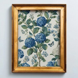 May include: A framed print featuring a botanical illustration of blue hydrangeas and butterflies on a cream background. The artwork is enclosed in a gold-colored wooden frame, creating a classic aesthetic.