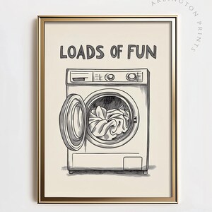 Könnte beinhalten: Eine Schwarzweißillustration einer Waschmaschine mit dem Text "Loads of Fun" darüber. Die Waschmaschine hat eine offene Tür und Wäsche im Inneren.