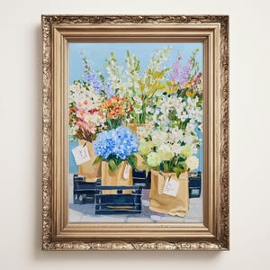 May include: A framed oil painting shows a flower market with diverse bouquets. The artwork features blue hydrangeas and other colorful flowers in brown paper bags and black crates, set against a light blue backdrop.