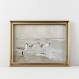 May include: A framed painting of four sandpipers standing on a beach with waves crashing in the background. The painting is done in muted tones of beige, brown, and white.