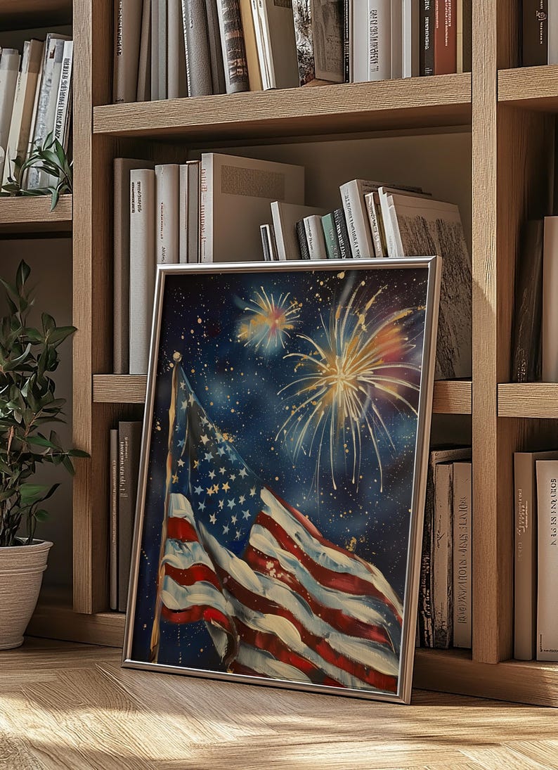 May include: A framed painting of an American flag waving in the wind with fireworks exploding in the night sky. The flag is red, white, and blue with stars on the blue field. The fireworks are yellow, orange, and red.