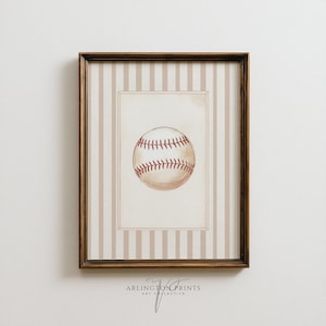 Puede incluir: Una impresión enmarcada de béisbol. La obra de arte presenta una ilustración en acuarela de una pelota de béisbol con costuras rojas. La impresión está sobre un fondo crema con un patrón de rayas y está encerrada en un marco de madera marrón. El texto "ARLINGTON PRINTS ART COLLECTIVE" está en la parte inferior.