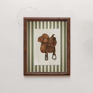 May include: A framed print showing a watercolour illustration of a brown leather saddle. The saddle is on a postage stamp-style background with a green and white striped pattern. The frame is dark brown, and the text "ARLINGTON PRINTS" is visible.