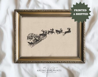 May include: Framed vintage-style print featuring Santa Claus in a sleigh pulled by reindeer. The black and white illustration is set against a cream background, within a gold-colored ornate frame. The print includes the text "PRINTED & SHIPPED".