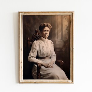 May include: A framed sepia-toned portrait of a woman seated in a wooden chair. She wears a light-colored dress with lace detailing and a high collar. The portrait is set against a dark, blurred background, and the frame is a light, distressed wood.