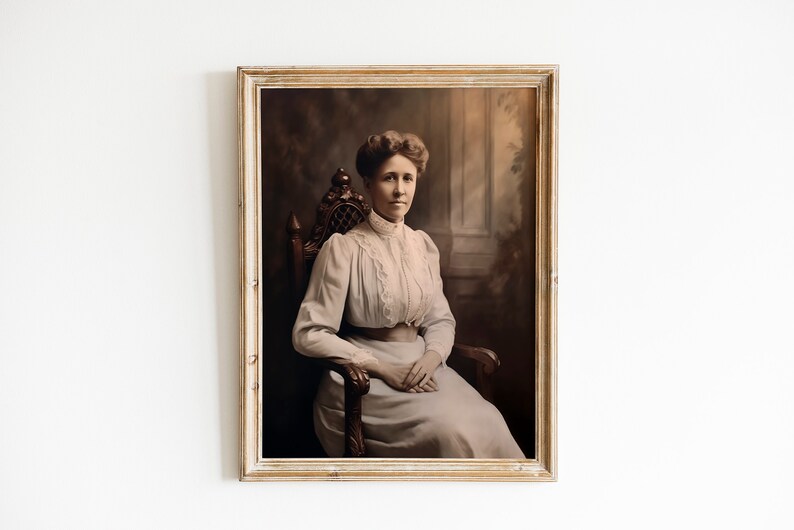 May include: A framed sepia-toned portrait of a woman seated in a wooden chair. She wears a light-colored dress with lace detailing and a high collar. The portrait is set against a dark, blurred background, and the frame is a light, distressed wood.