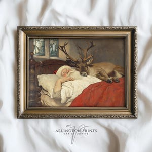 May include: A framed art print titled ARLINGTON PRINTS ART COLLECTIVE depicting a painting of a person with a white beard and red hat sleeping in a bed with a reindeer resting its head on the person's shoulder under a red blanket.
