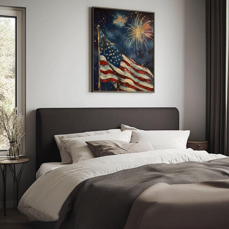 May include: A dark gray upholstered headboard with white and beige pillows on a bed with a gray blanket. A framed print of an American flag waving in the wind with fireworks in the background hangs on the wall above the headboard.