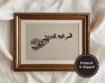 May include: Framed vintage-style print featuring Santa Claus in a sleigh pulled by reindeer. The black and white illustration is set against a neutral background, framed in a gold-colored ornate frame. The print is a festive holiday decoration.