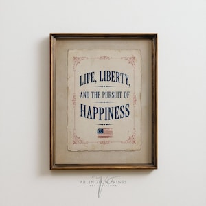 May include: A framed wall art print featuring the text LIFE, LIBERTY, AND THE PURSUIT OF HAPPINESS in blue serif font on a beige, aged-paper background. The design includes red decorative scrollwork borders and a small American flag icon.