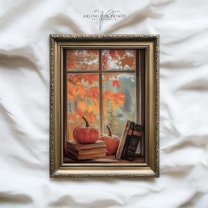 May include: A framed autumn-themed print featuring a window view with pumpkins, books, and fall foliage. The artwork has a gold-colored frame and the text "ARLINGTON PRINTS ART COLLECTIVE" in the top center.
