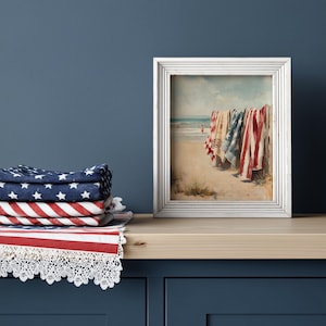 Beach scene with red, white, and blue towels hanging on a wooden fence, ocean waves and swimmers in the background. Coastal Americana style perfect for summer or 4th of July decor. Patriotic Beachy Wall Art, Coastal 4th of July PRINTABLE, Red White Blue Beach Towels, Vintage Summer Seaside Decor, Retro Americana Print