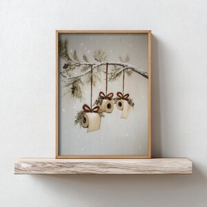 Funny Christmas bathroom print featuring toilet paper ornaments with red bows and greenery on a snowy pine branch, humorous holiday wall art digital download.