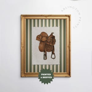 Printed Western wall art featuring a detailed illustration of a vintage leather cowboy saddle with stirrups, displayed on textured parchment-style paper with a striped green and cream background. Ideal for rustic home decor, ranch houses, barns, or cowboy-themed rooms. This artwork evokes classic Western heritage and equestrian charm, making it a perfect printed piece for lovers of country and cowboy style.
