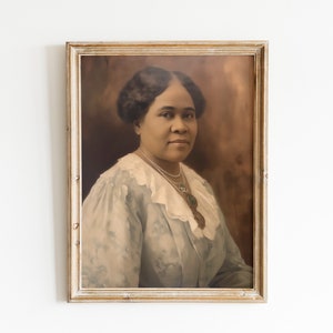 May include: A framed portrait of a woman with dark hair and a light blue dress with a white lace collar. The portrait is in a vintage-style, light-colored wooden frame, hanging on a white wall. The image has a sepia tone.