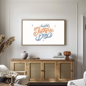 May include: A framed art print with the words "Happy Father's Day" in orange and blue script. The artwork is displayed above a wooden cabinet with woven door panels. Decorative items include a vase and a small sculpture.