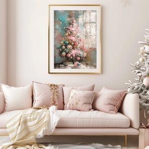 May include: A pink and white sofa with gold throw pillows and a blanket. A framed painting of a pink and green Christmas tree with ornaments hangs on the wall behind the sofa. A white flocked Christmas tree with ornaments is in the background.