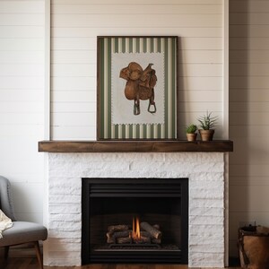 Printed Western wall art featuring a detailed illustration of a vintage leather cowboy saddle with stirrups, displayed on textured parchment-style paper with a striped green and cream background. Ideal for rustic home decor, ranch houses, barns, or cowboy-themed rooms. This artwork evokes classic Western heritage and equestrian charm, making it a perfect printed piece for lovers of country and cowboy style.