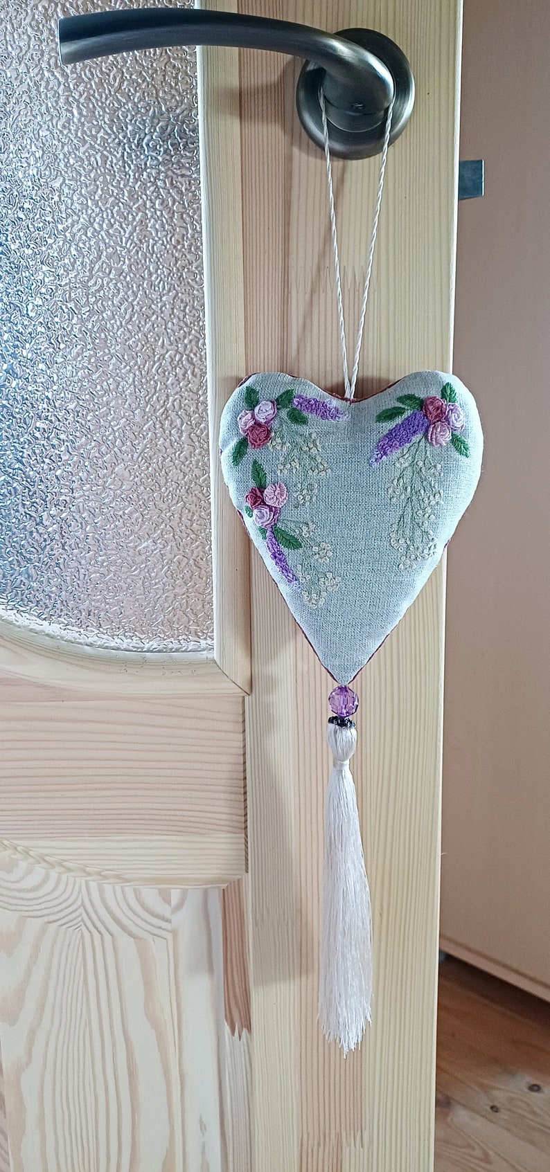 Handmade embroidered linen heart shaped home decor sachet, with hanging loop and tassel. Hung on a door hanger.
