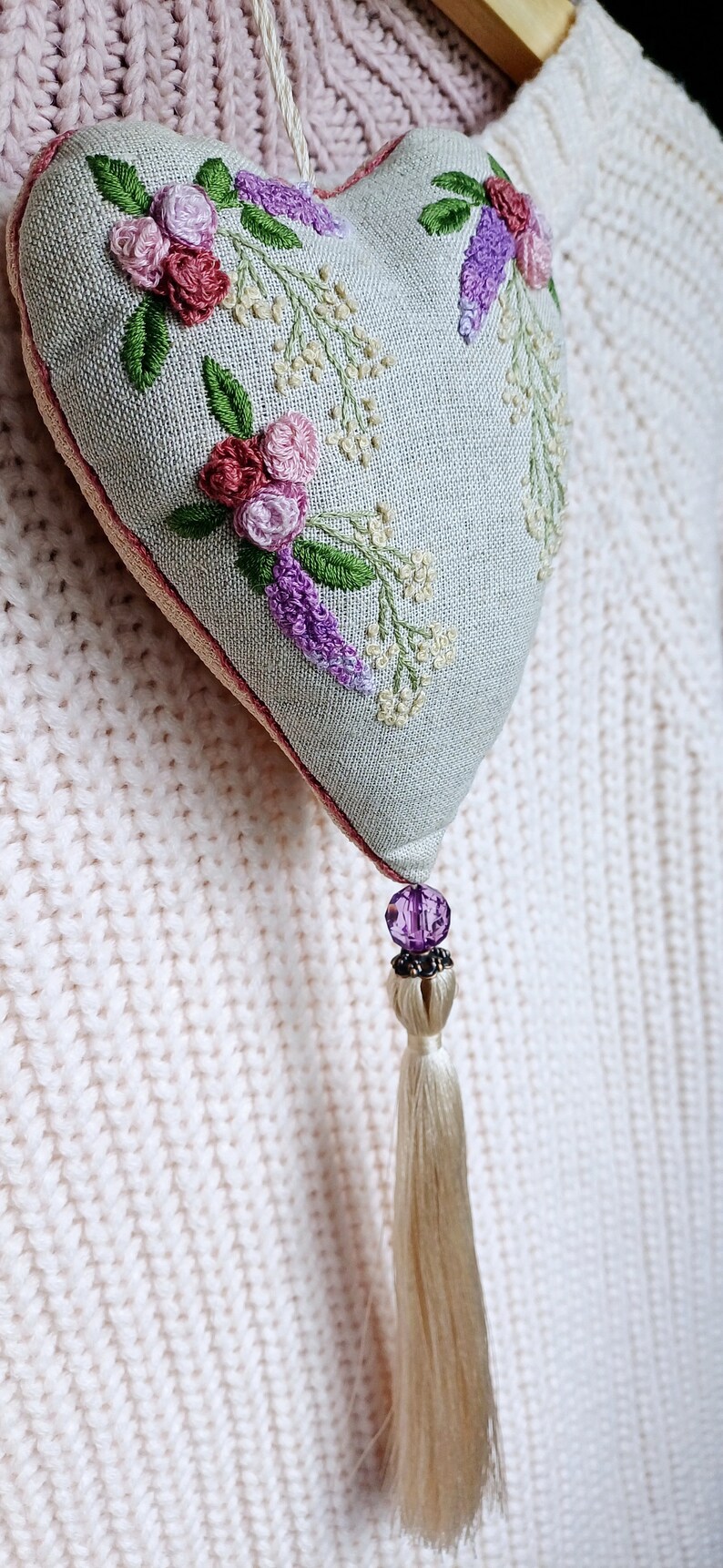 Handmade embroidered linen heart shaped home decor sachet, with hanging loop and tassel. Hung on a clothes hanger.
