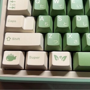 May include: A green and white keyboard with Japanese characters on the keys. The keys have various symbols, including a teapot, a leaf, and the word "Super".