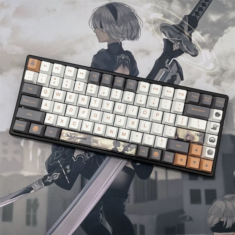 May include: A black and white mechanical keyboard with custom keycaps featuring a video game theme. The keycaps are white, gray, and orange with custom graphics and text. The keyboard is set against a blurred anime-style background.