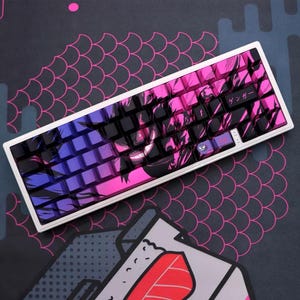 May include: A white mechanical keyboard with keycaps in purple, pink, and black. The keycaps have a gradient design and a character graphic. The keyboard sits on a patterned surface.