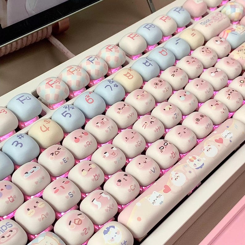 May include: A pink and white keyboard with cute cartoon animal keycaps. The keycaps feature various animals, including cats, dogs, and bunnies. The keyboard also has a pink and white space bar with a heart design.