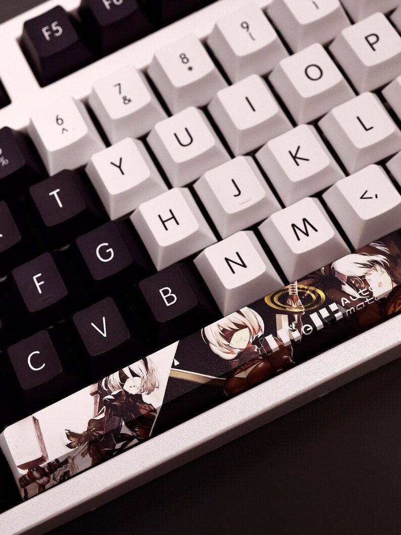 K&ouml;nnte beinhalten: Eine wei&szlig;e mechanische Tastatur mit schwarzen Tastenkappen. Die Tastatur verf&uuml;gt &uuml;ber einen benutzerdefinierten Tastenkappensatz mit einem gedruckten Bild eines Videospielcharakters. Die Tastenkappen sind mit Buchstaben, Zahlen und Symbolen beschriftet. Die Tastatur hat ein wei&szlig;-schwarzes Farbschema.