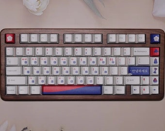 Könnte beinhalten: Eine Tastatur in voller Größe mit einem Holzrahmen und weißen Tasten. Die Tastatur hat ein koreanisches Tastaturlayout mit einem rot-weiß-blauen Akzentstreifen. Die Leertaste hat den koreanischen Text "안녕하세요", der ins Deutsche mit "Hallo" übersetzt wird.