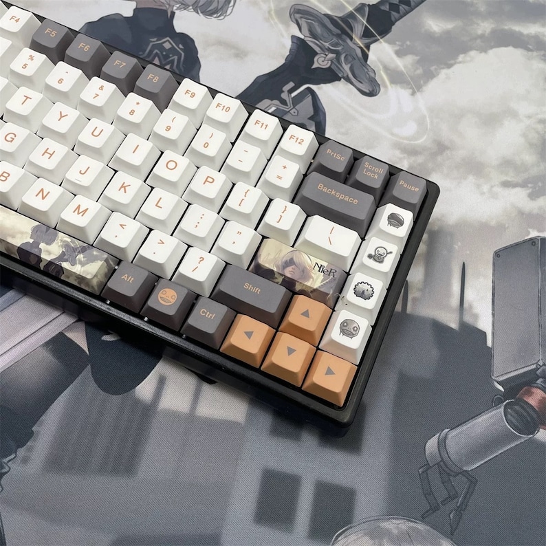 May include: A mechanical keyboard with white, gray, and orange keycaps. The keyboard features custom keycaps with anime-style artwork and the text "NieR". The keyboard is on a gray and white patterned surface.